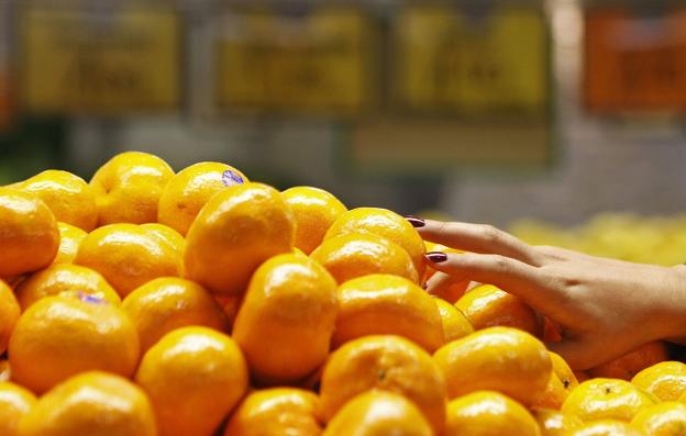 Una consumidora elige en la frutería las mandarinas que quiere comprar. / daniel muñoz/reuters