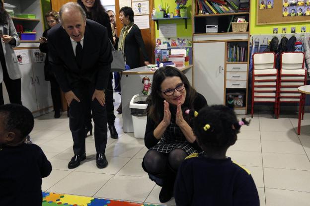 La consellera Mónica Oltra juega con una niña de la escuela infantil de Casa Caridad junto al presidente Luis Miralles, ayer. / irene marsilla