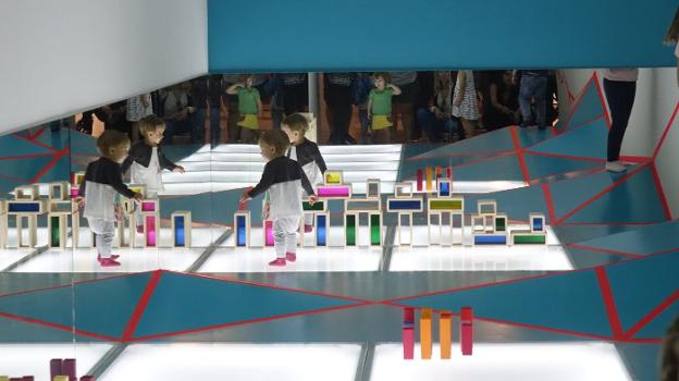 Un bebé experimenta con formas geométricas sobre una superficie de volúmenes, con luces y espejos en el Espai de Telles de Castellón. / lp