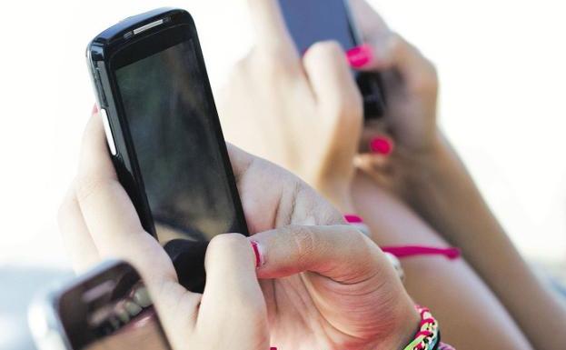 Varias jóvenes chatean con sus teléfonos móviles. / josep M. suria