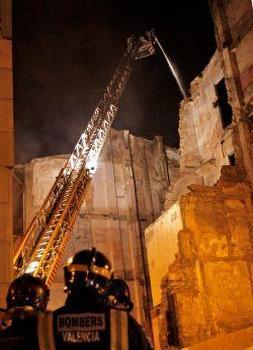 Varios bomberos observan como sus compañeros lanzan agua desde el brazo de una grua sobre el tejado del edificio en el número seis de la calle Murillo de Valencia que esta noche ha sufrido un incendio por causas que se desconcen. El incendio afectó al teatro Princesa, colindante con el inmueble siniestrado. FOTO EFE./