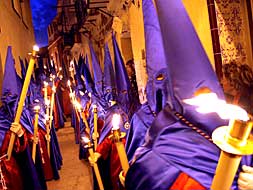 Un grupo de nazarenos recorre una de las calles del centro de Alicante con velas./