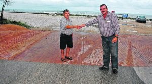 VECINOS. Dos residentes en la playa de l'Almadrava se estrechan la mano en la calle que divide los términos de Dénia (izquierda) y Els Poblets (derecha). /JOSÉ IGLESIAS/